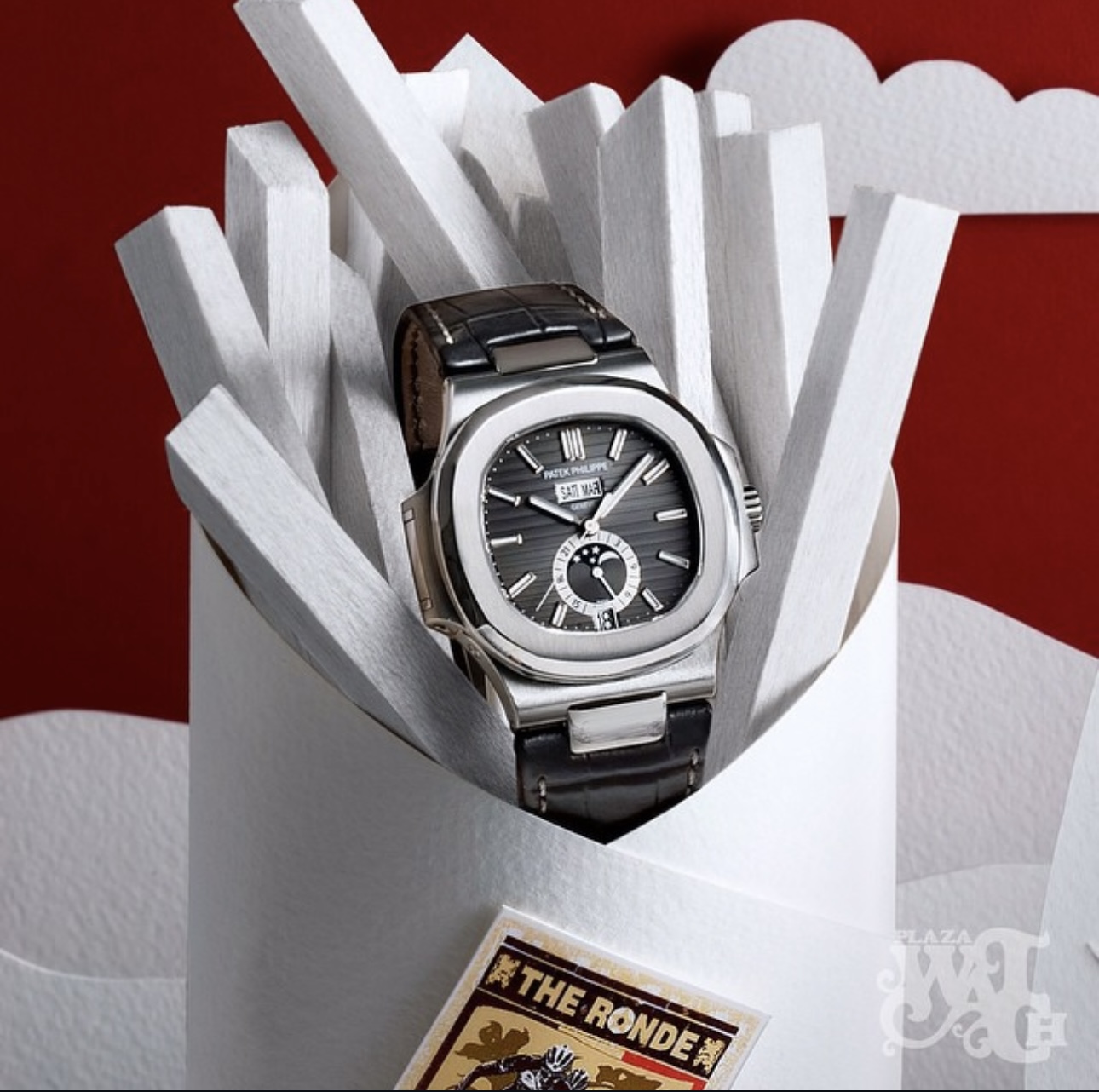 Patek Philippe-klocka i ett arrangemang med vitt papper och röd bakgrund